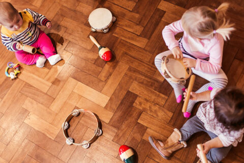Kolme lasta istuu lattialla eri musiikkivälineiden kanssa.