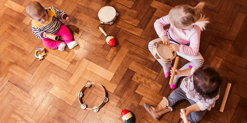Kolme lasta istuu lattialla eri musiikkivälineiden kanssa.