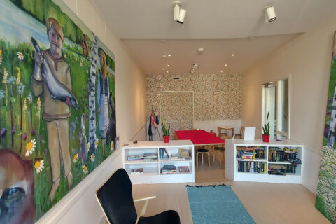Huone, jossa kaksi kirjahyllyä rajaa tilan kahteen osaan, vasemmalla seinällä iso maalaus.